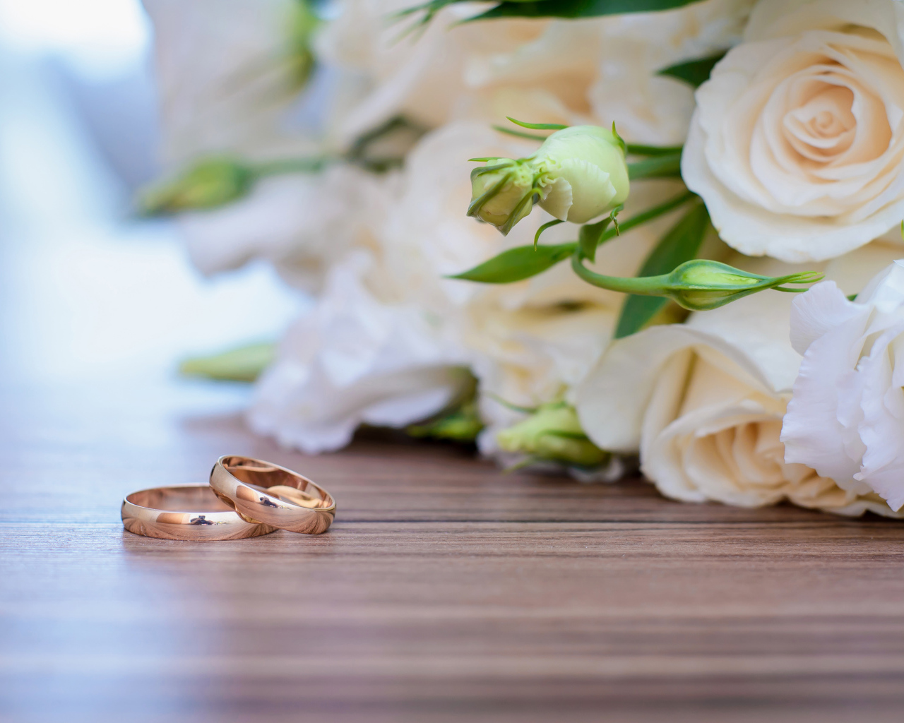 Букет белых роз на столе с золотыми обручальными кольцами
