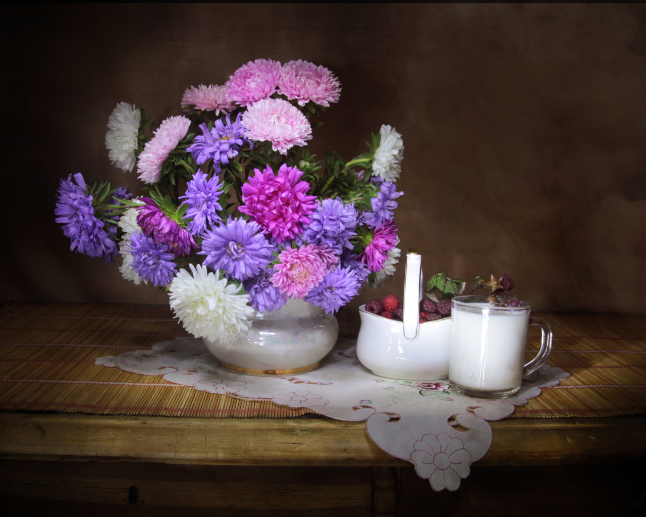 Букет разноцветных астр в вазе на столе с молоком и ягодами малины