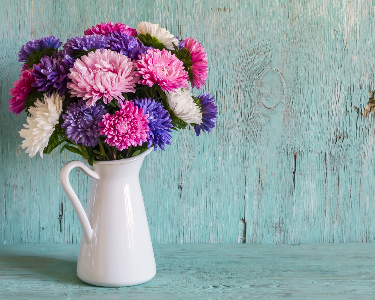 Разноцветные астры в вазе на деревянном фоне