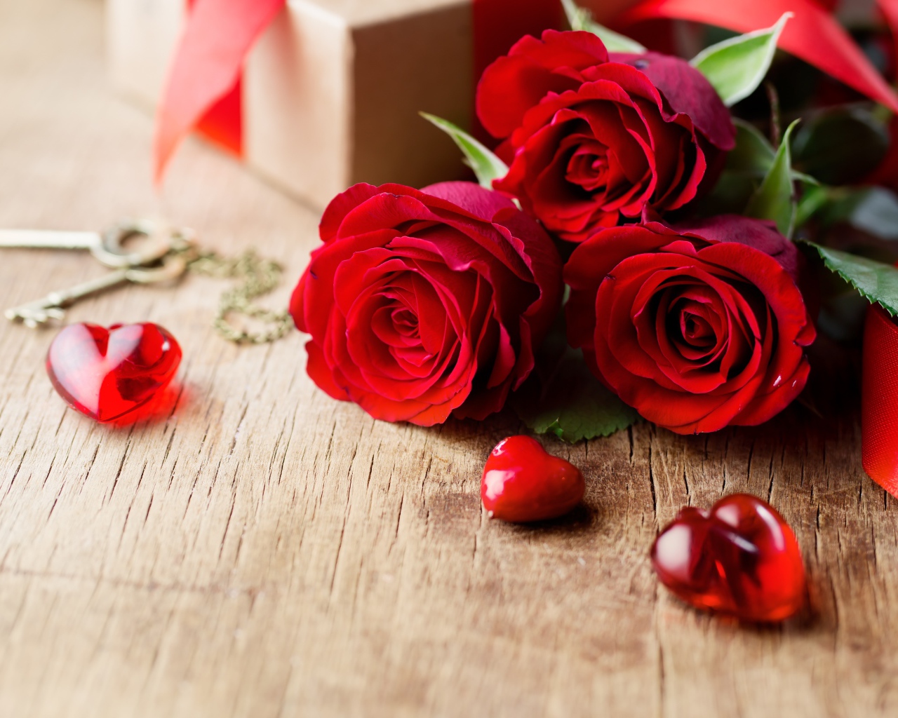 Три красных розы на деревянном столе с красными сердечками