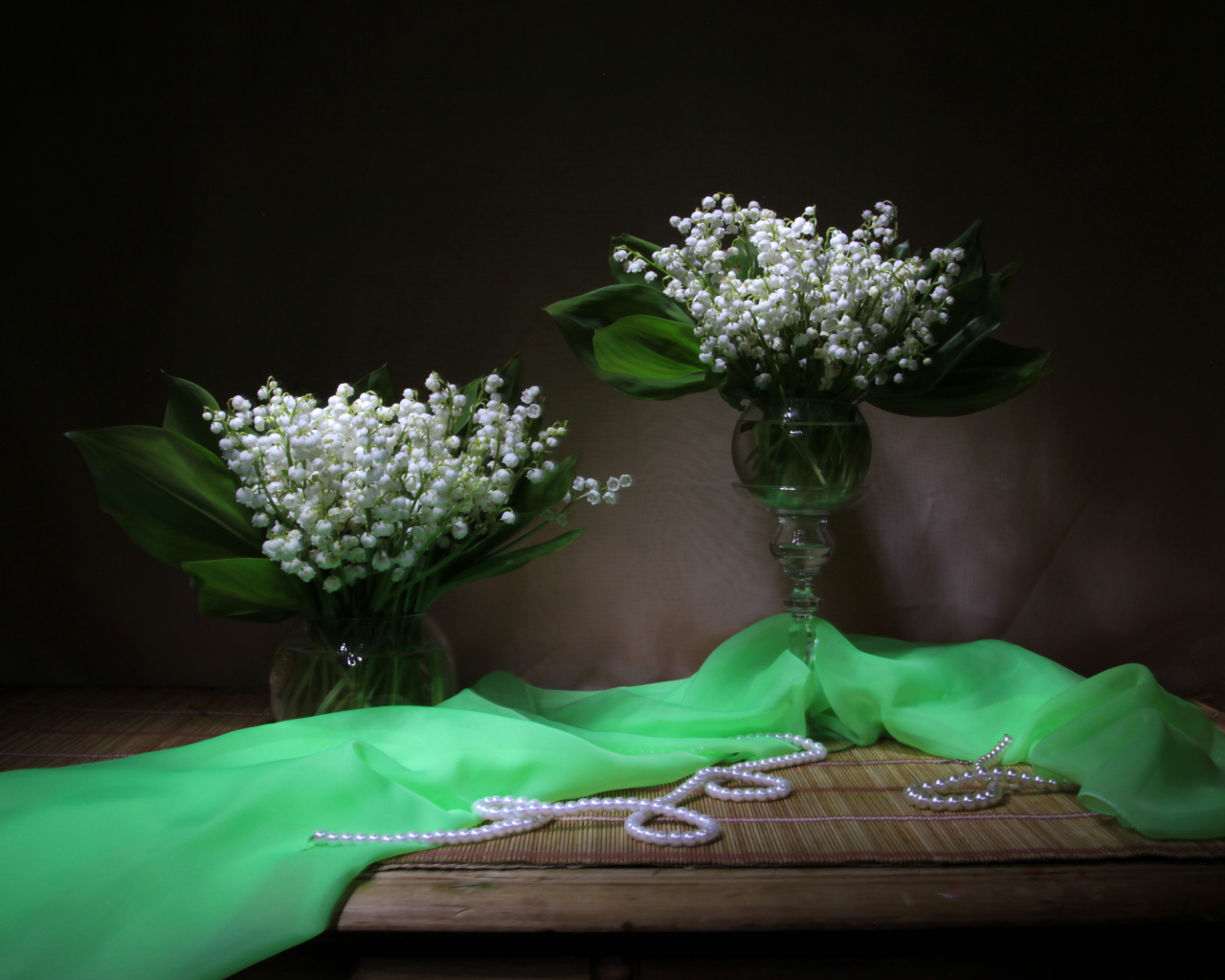 Два букета ландышей с бусами на столе 