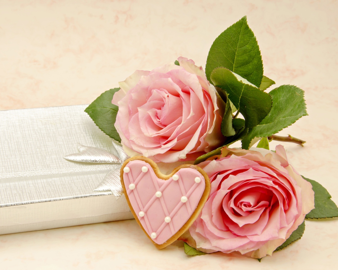 Две розовые розы с печеньем в виде сердца на розовом фоне