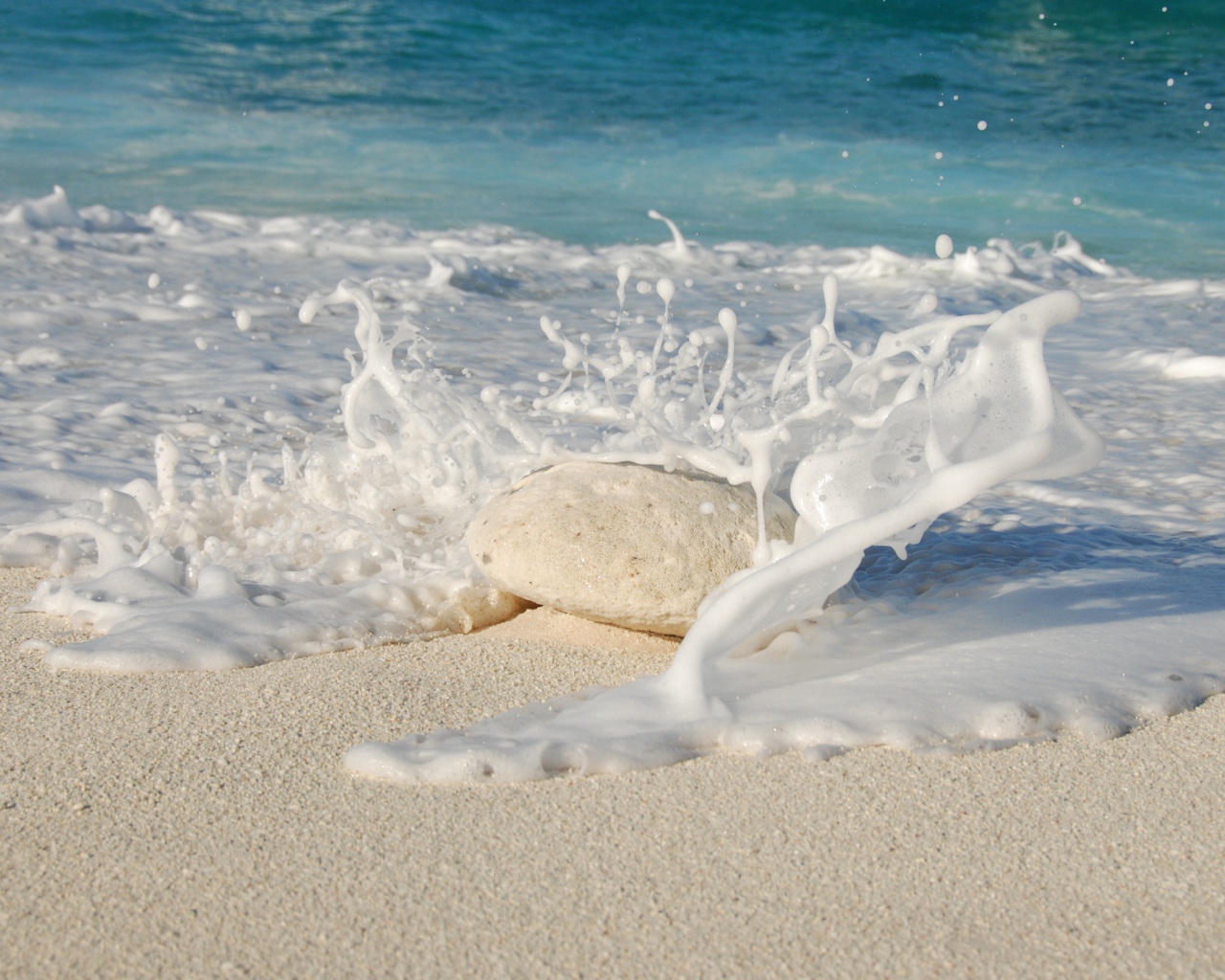 Белые морские волны бьются об камень на желтом песке