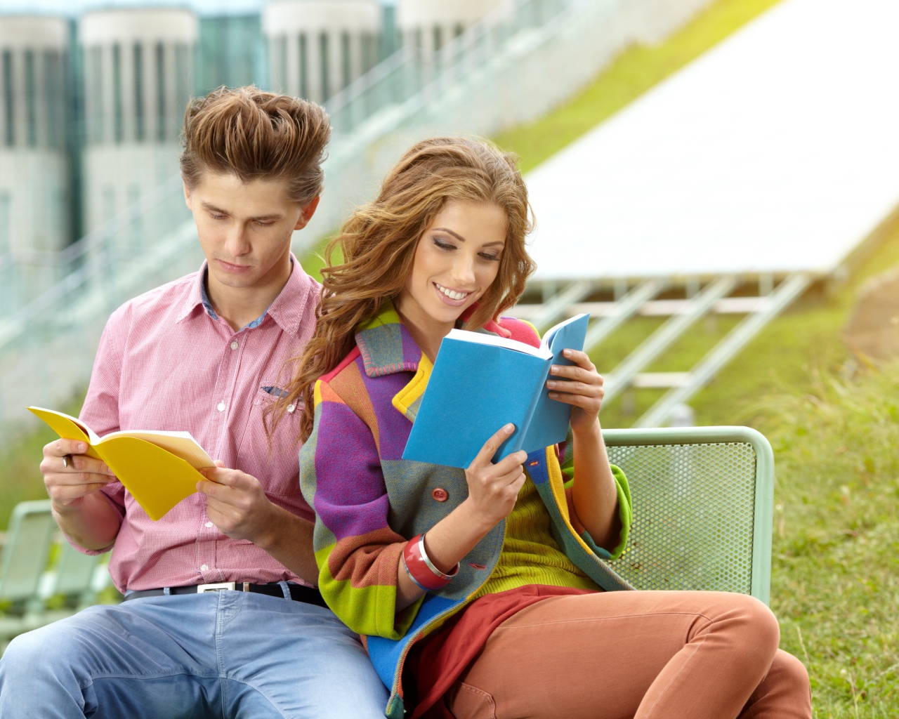 A guy and a girl are reading books sitting on a bench