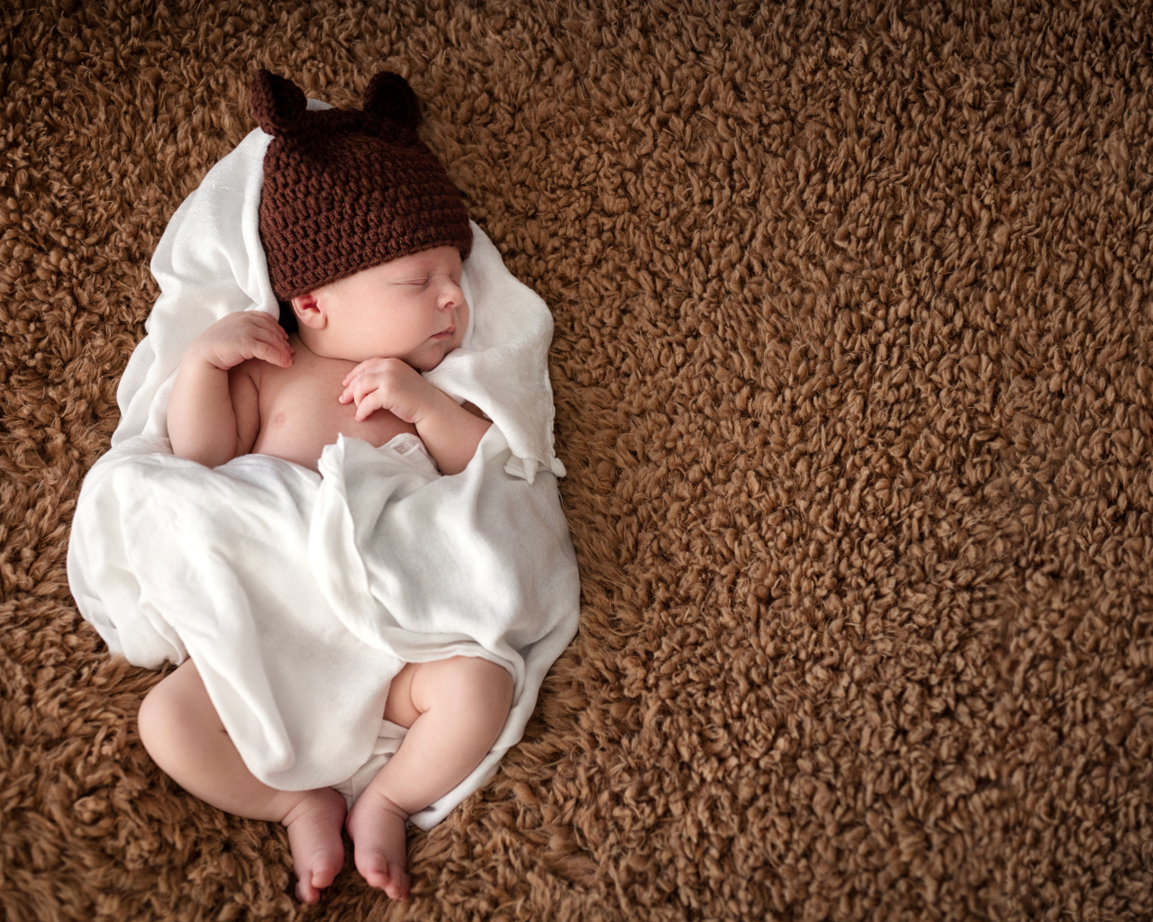 Грудной ребенок в вязаной шапке  спит в белом покрывале 