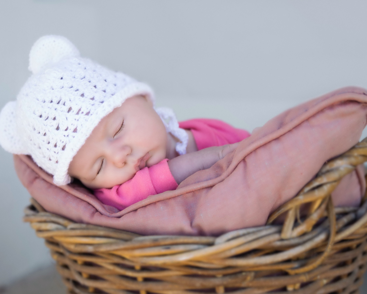 Маленький ребенок в белой шапке спит в корзине