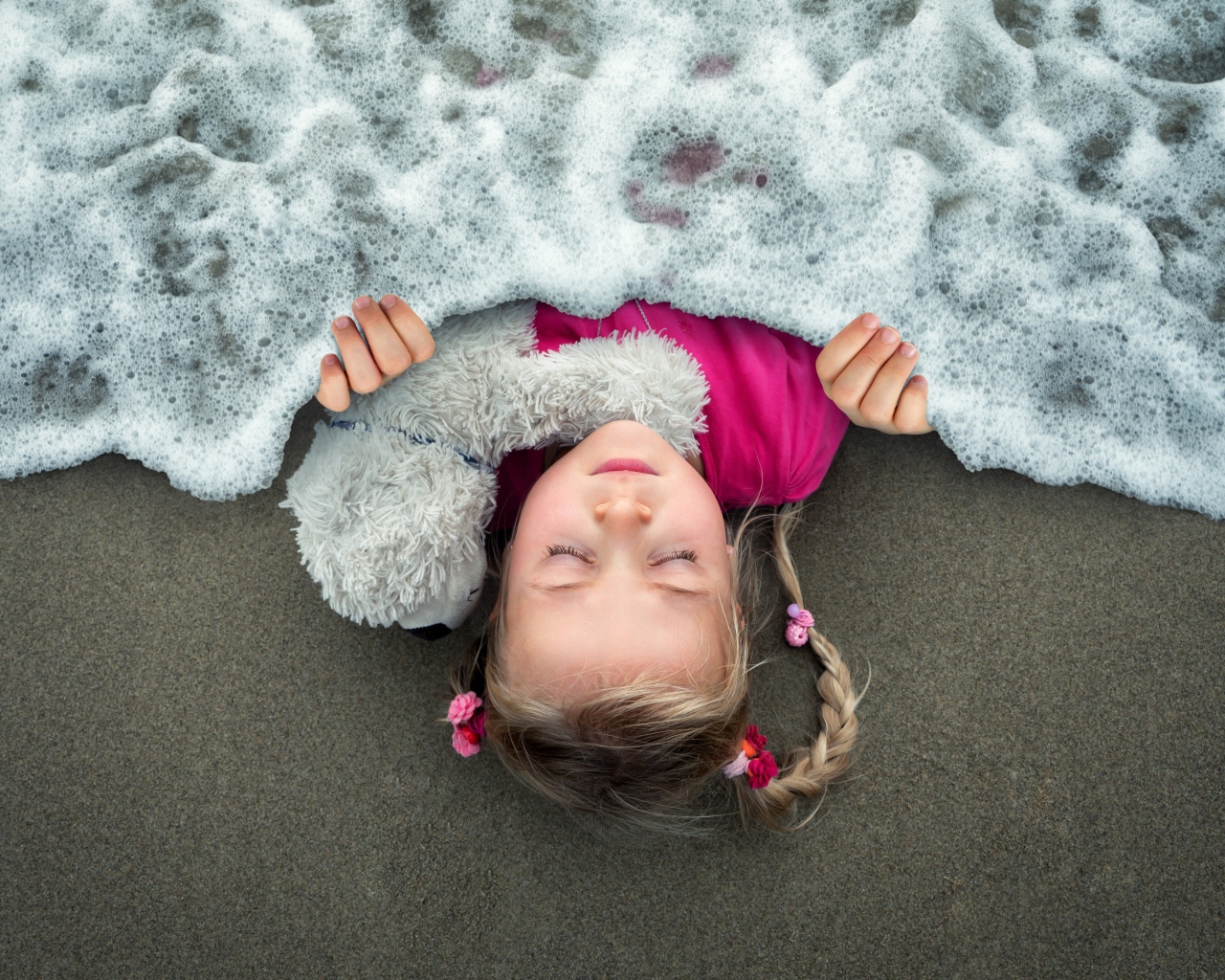 Маленькая девочка спит на песке под одеялом из морской пены