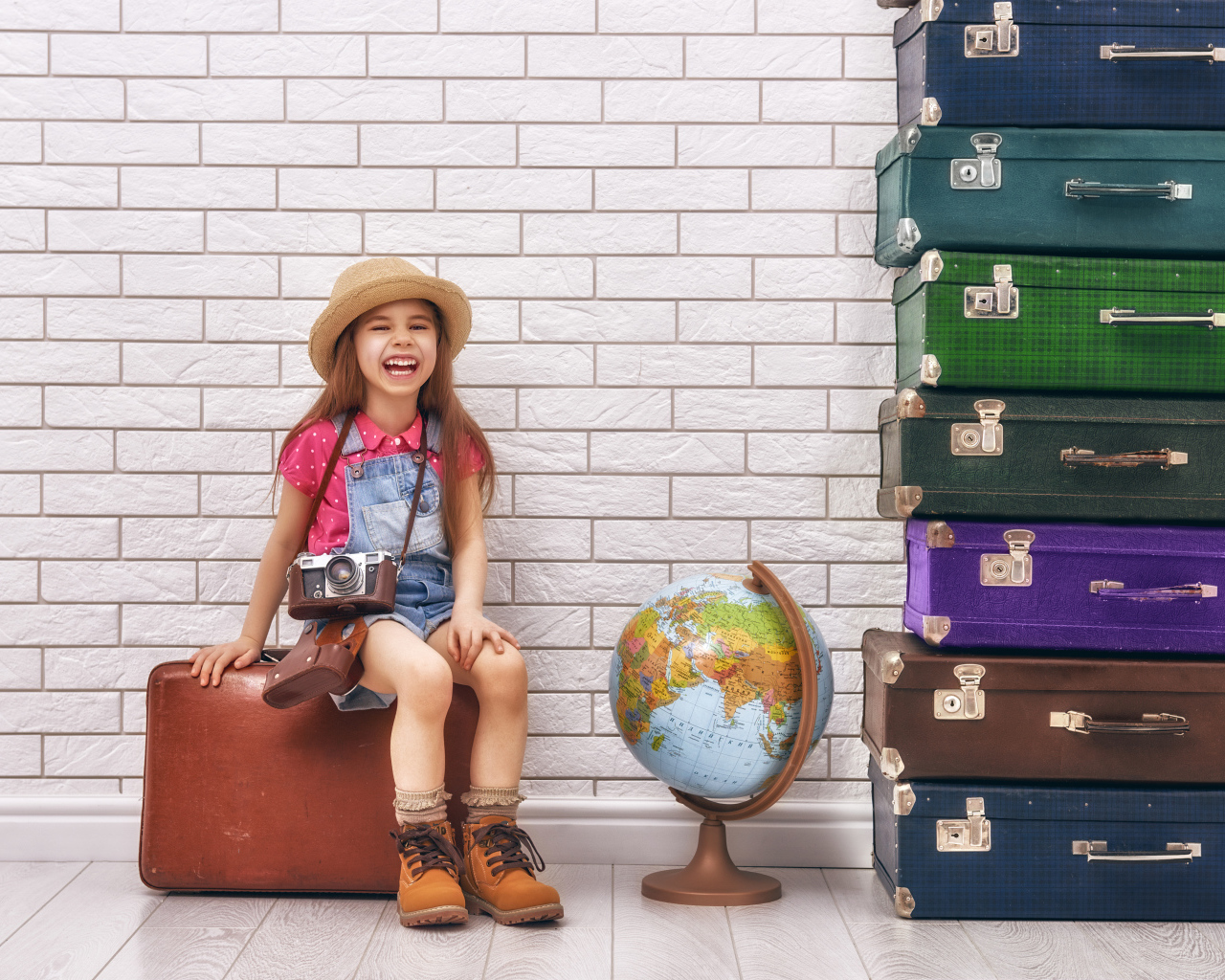 Маленькая девочка с фотоаппаратом сидит на чемодане