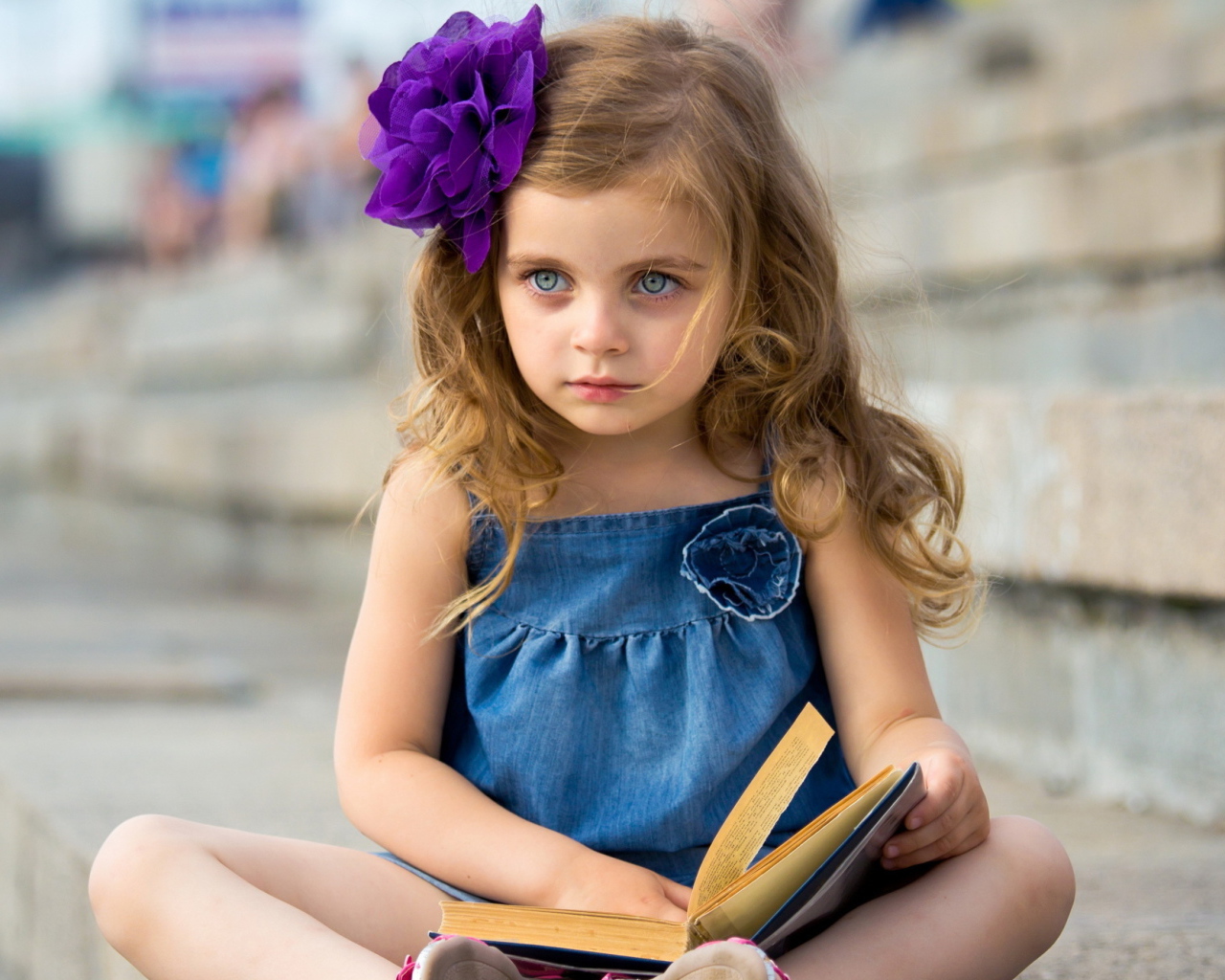 Маленькая девочка с цветком в волосах сидит на ступенях