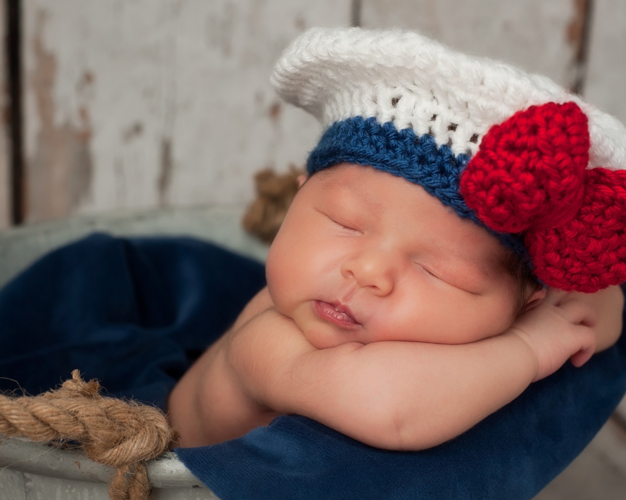 Спящий грудной ребенок в вязаной шапочке с красным бантом