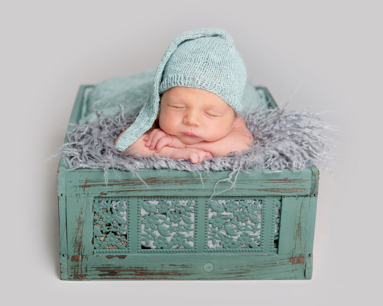 Спящий ребенок в зеленом ящике на сером фоне