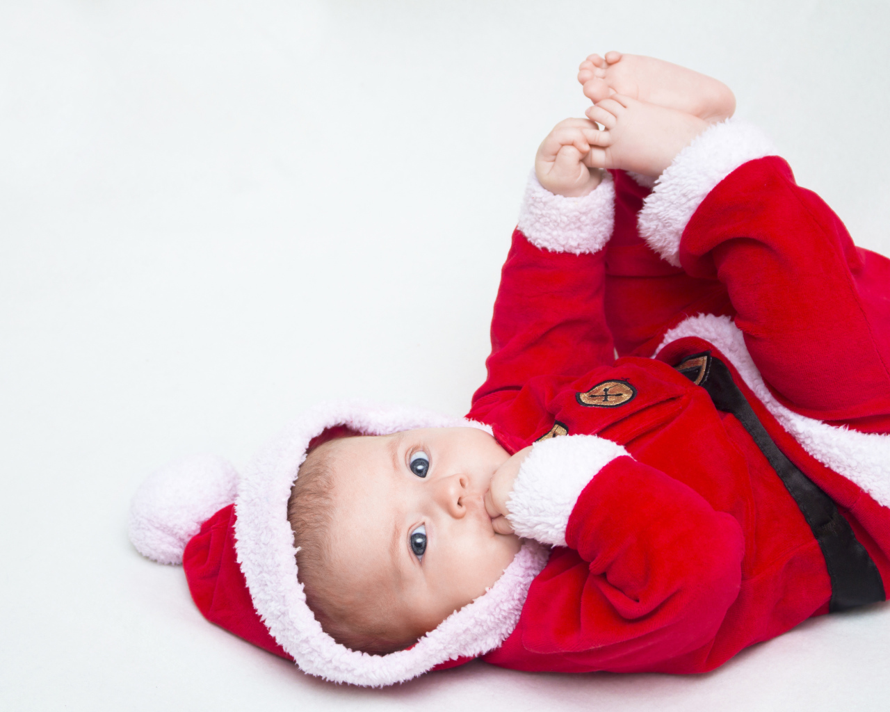 Маленький ребенок в красном новогоднем костюме на сером фоне