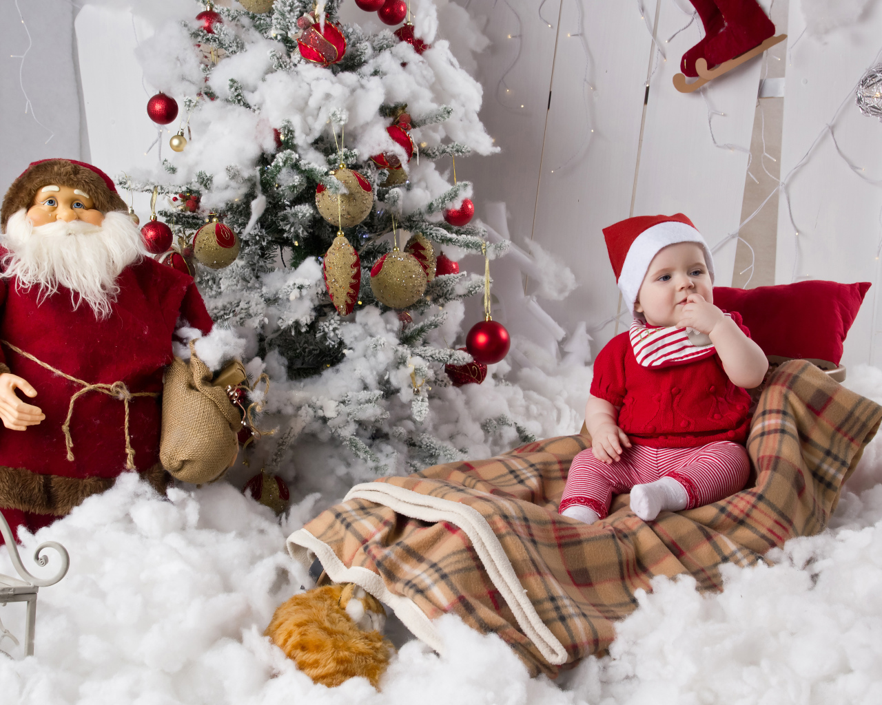 Маленький ребенок в санях у елки с дедом морозом на Новый год 