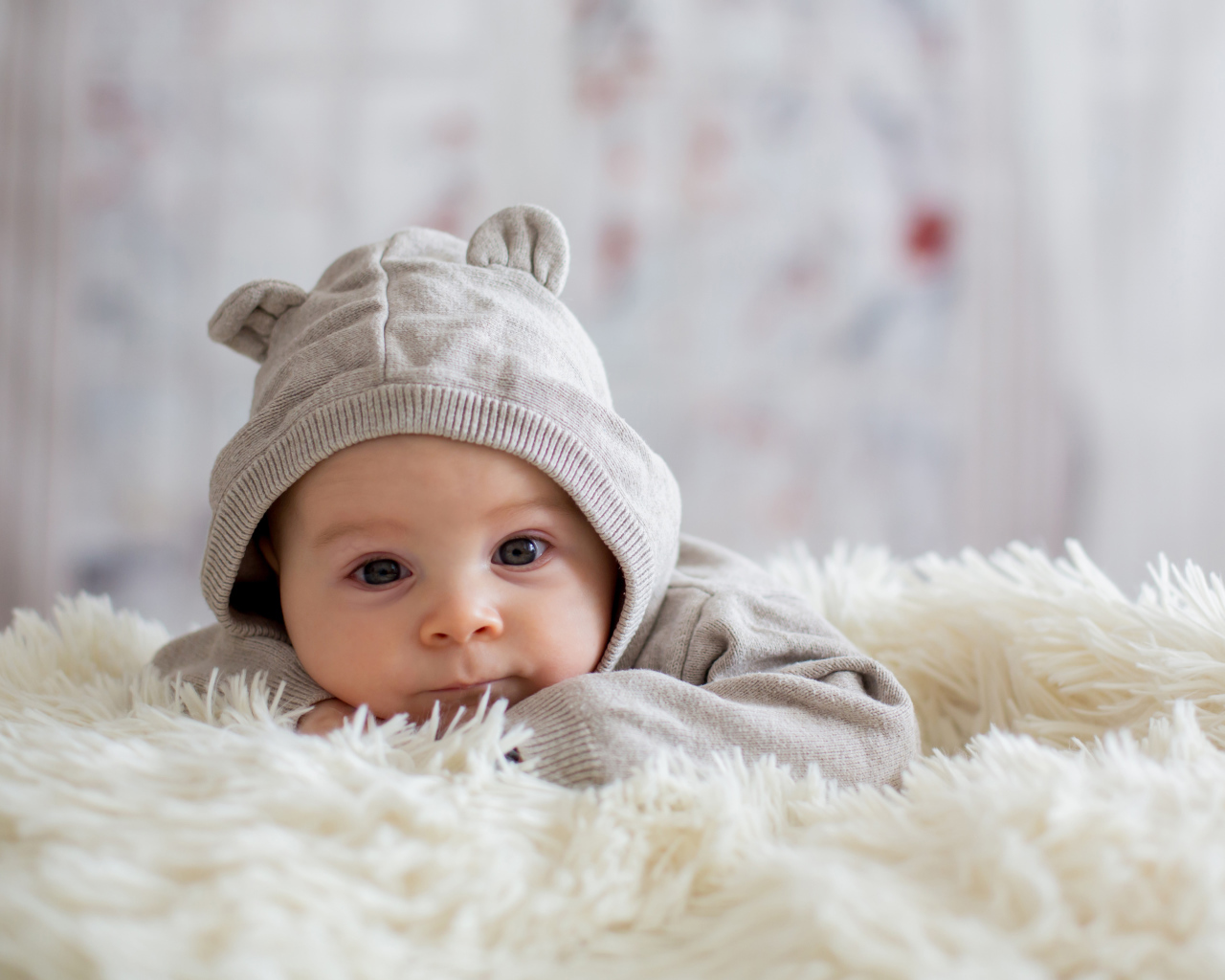 Маленький ребенок лежит на белом меховом покрывале 