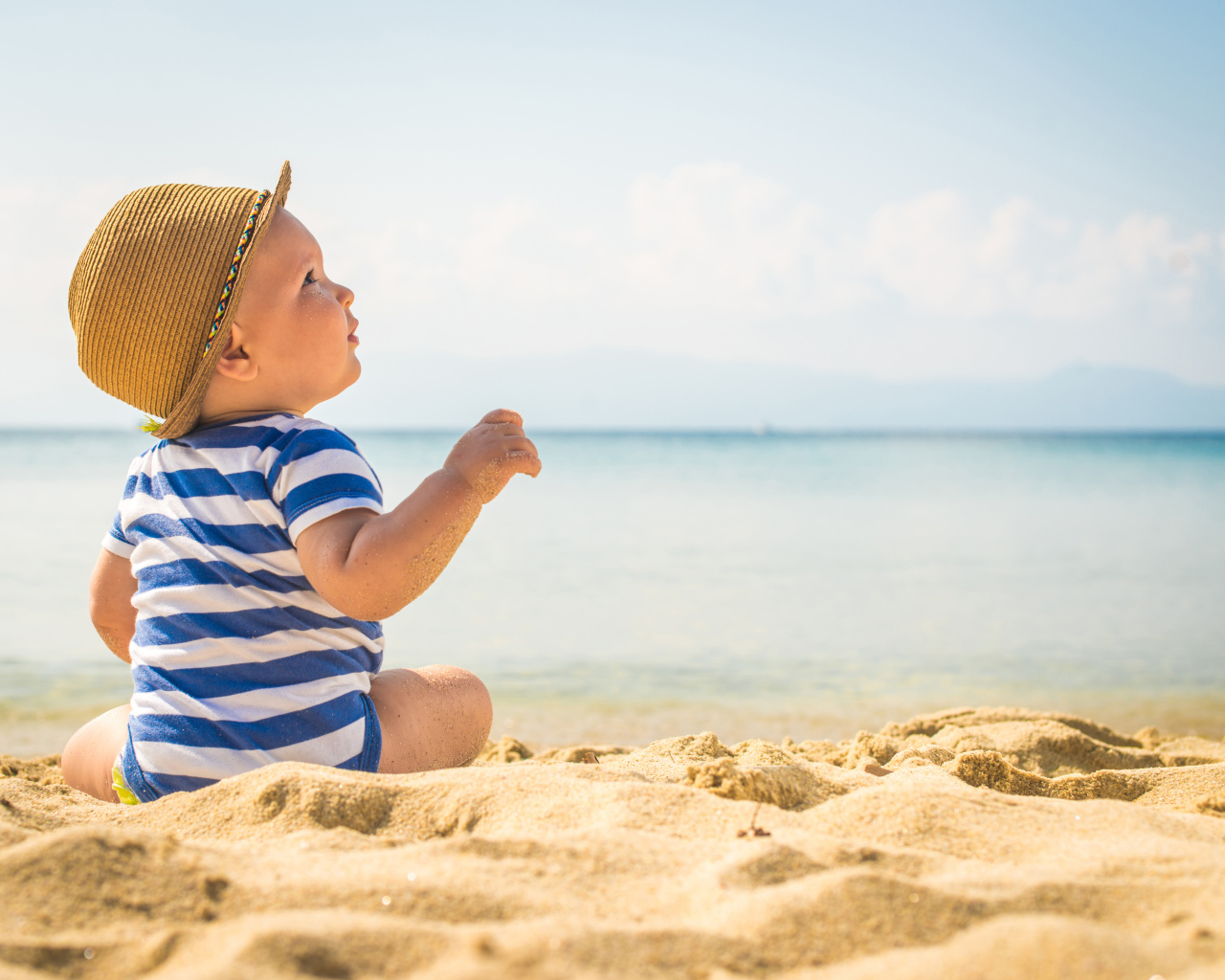 Маленький ребенок сидит на песке на пляже у моря