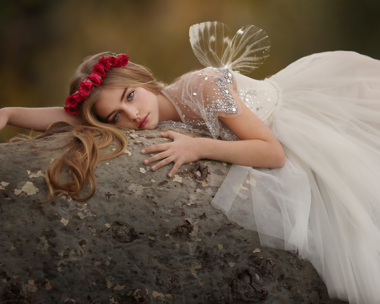 Красивая маленькая девочка в белом платье лежит на камне
