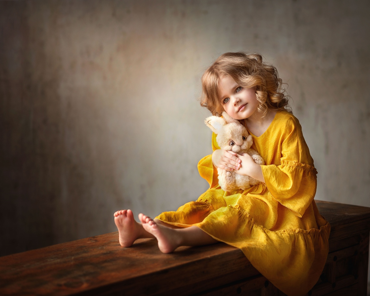 Красивая маленькая девочка в желтом платье с игрушкой