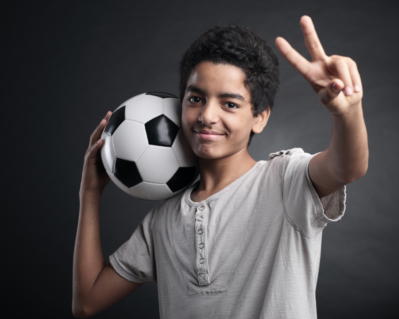 Мальчик с футбольным мячом на плече на сером фоне