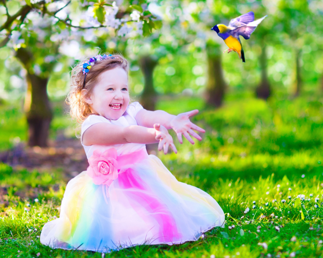 Смеющаяся маленькая девочка в красивом платье на зеленой траве