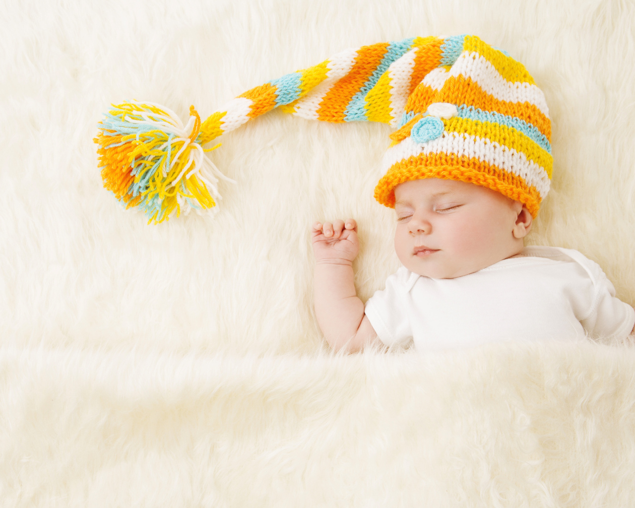 Маленький спящий под меховым покрывалом малыш в вязаной шапке