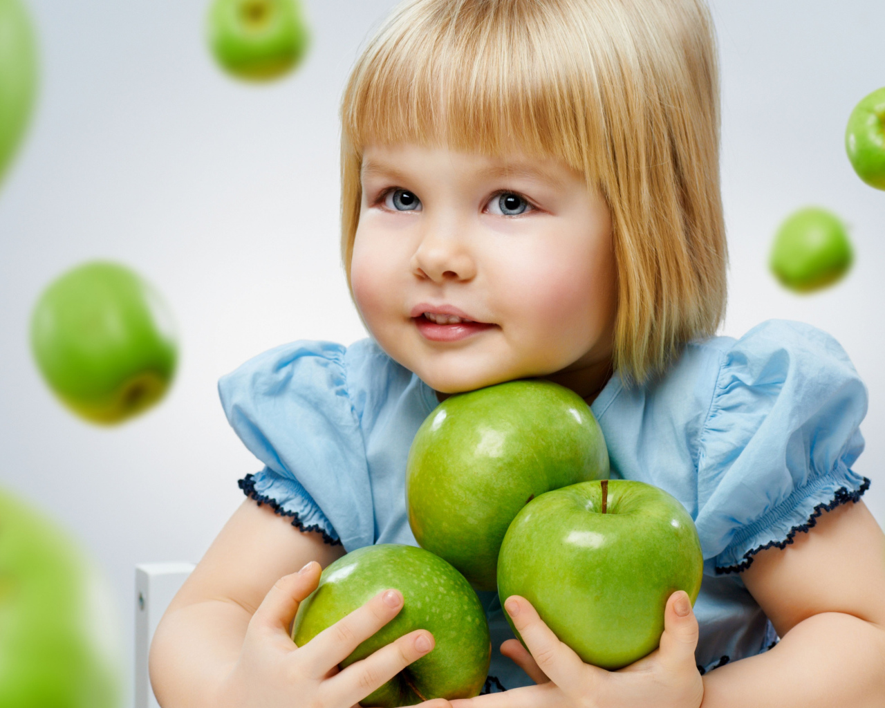 Маленькая девочка блондинка с зелеными яблоками