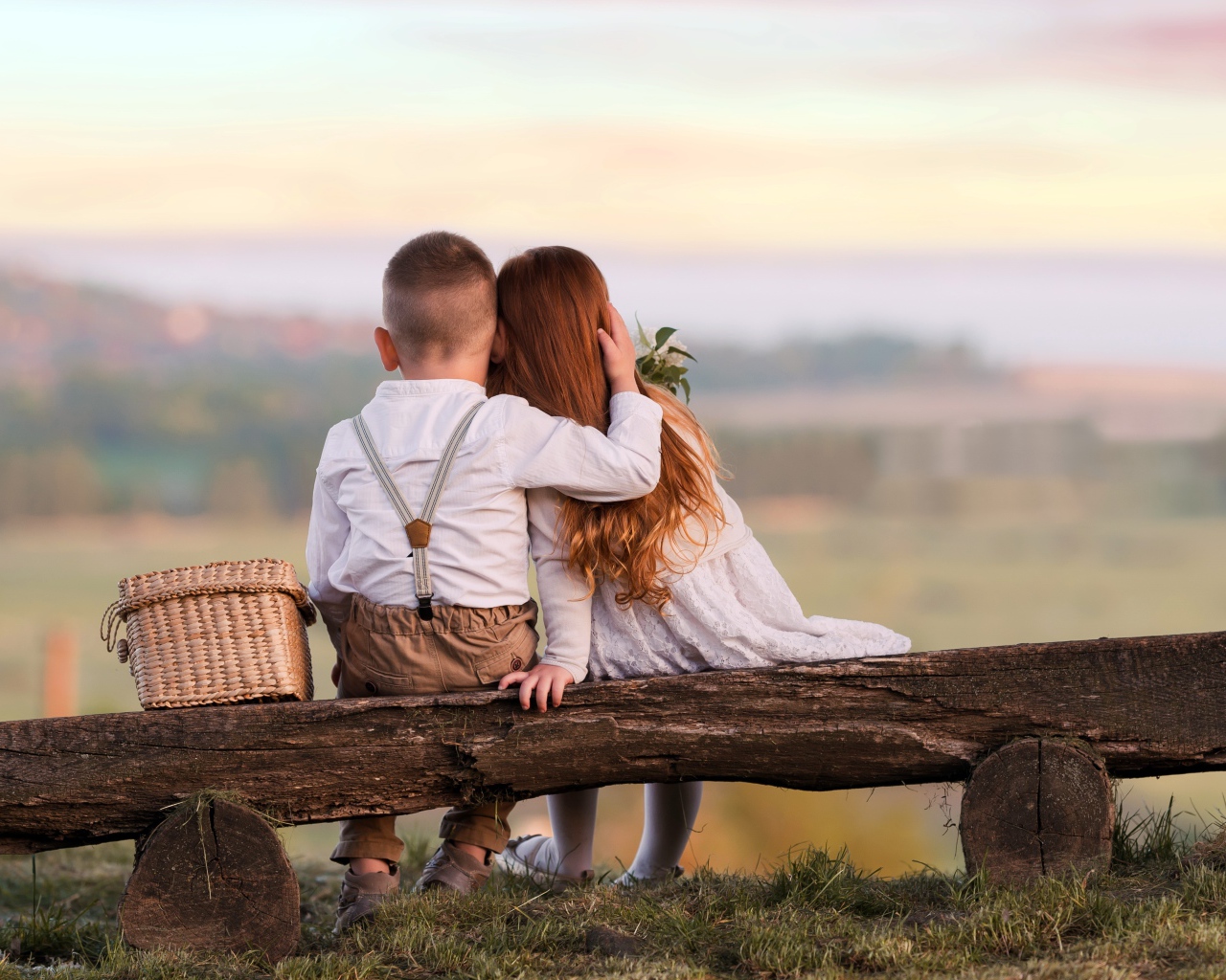 Маленькие мальчик и девочка обнимают друг друга на лавке