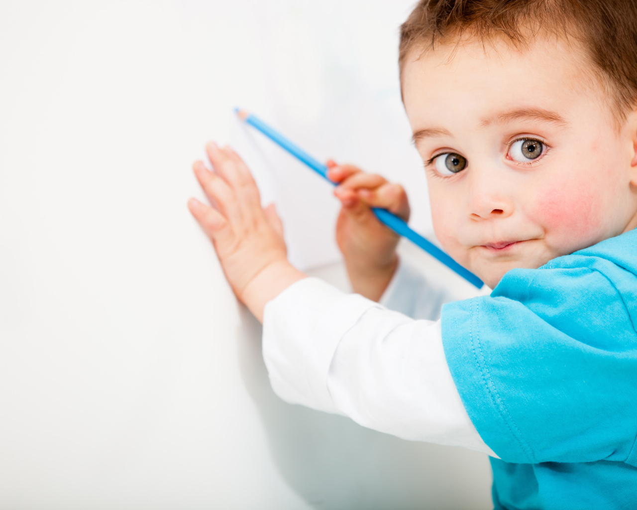 Маленький мальчик рисует карандашом на стене