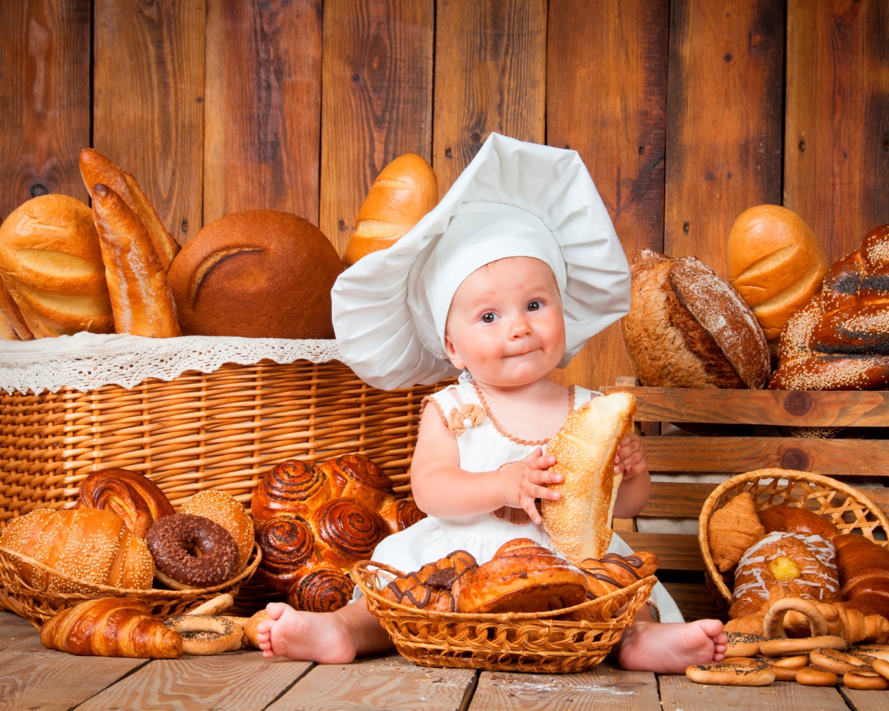 Маленький мальчик в костюме повара сидит на столе с выпечкой