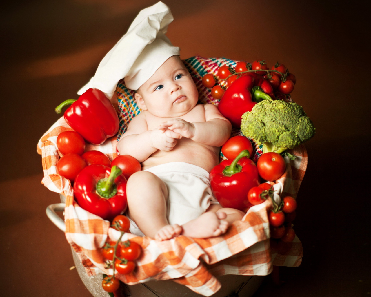Маленький мальчик в костюме повара в корзине с перцем и помидорами