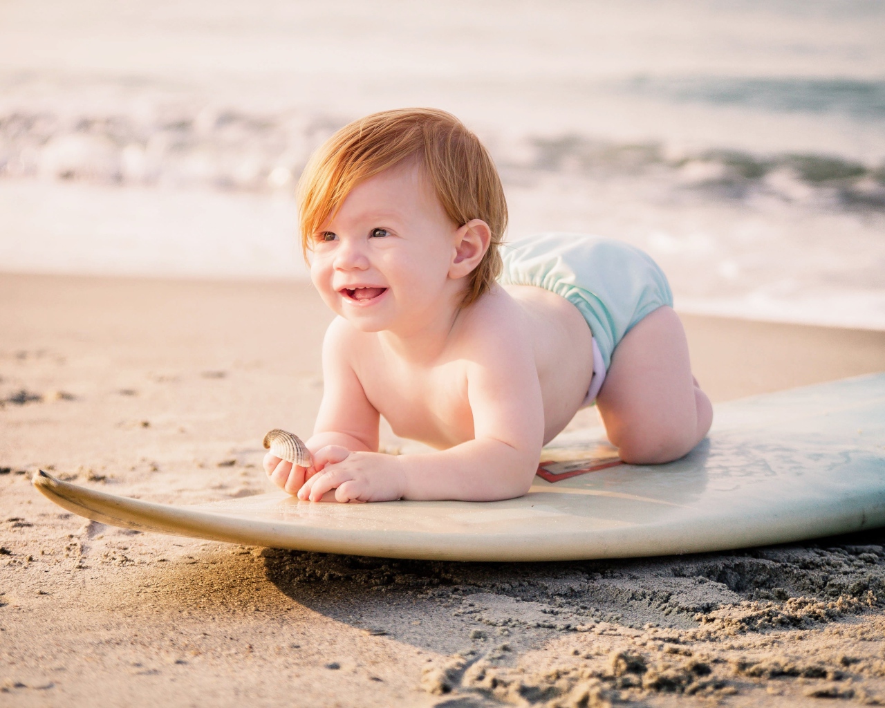 Маленький мальчик на доске для серфинга на пляже