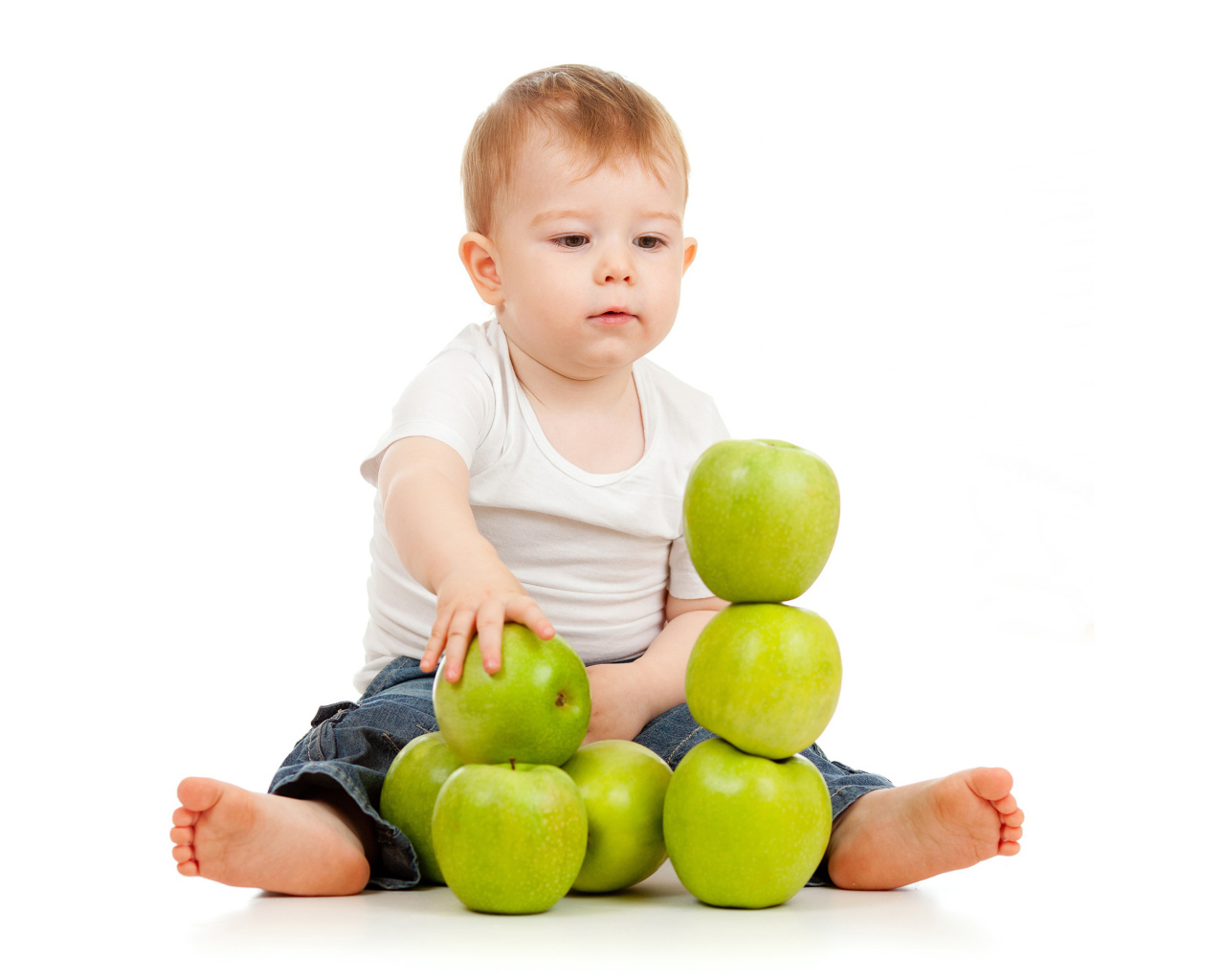 Маленький мальчик играет с зелеными яблоками на белом фоне
