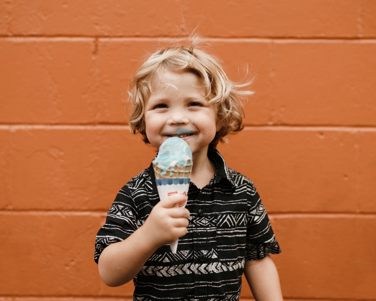 Маленький мальчик с мороженым в руках у стены