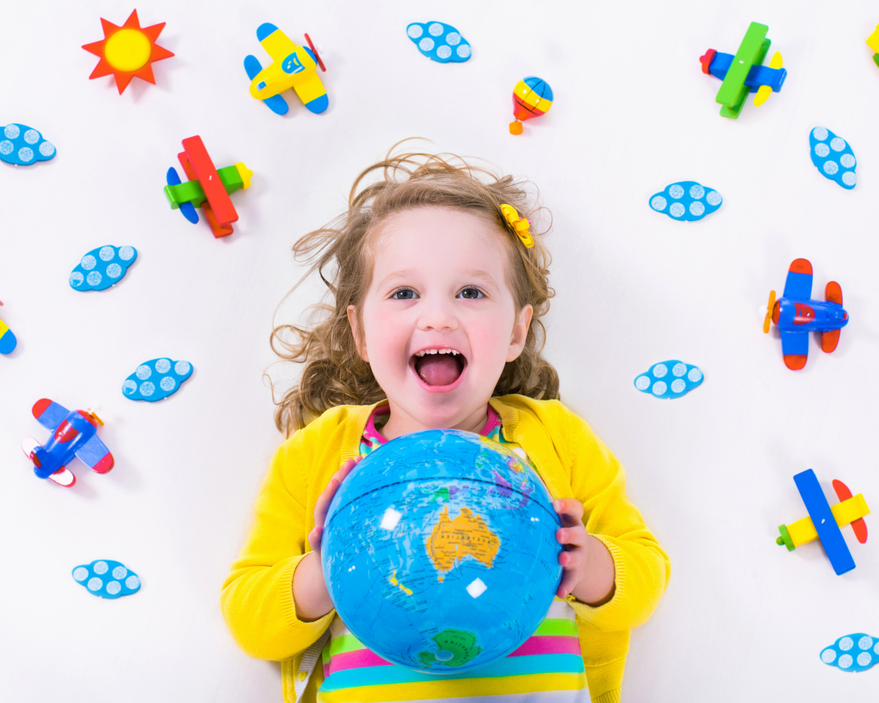 Маленькая веселая девочка с глобусом в руках 