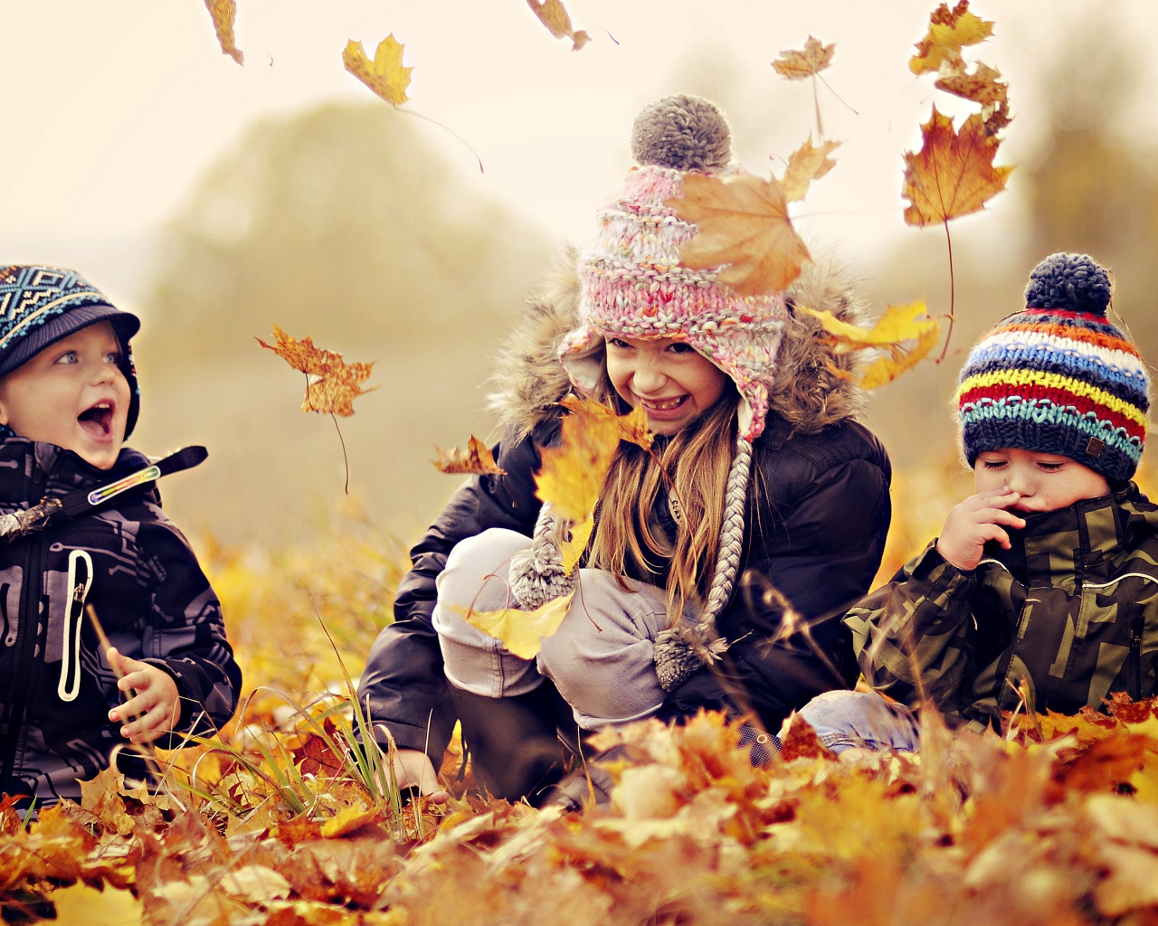 Маленькие дети играют на опавшей желтой листве осенью