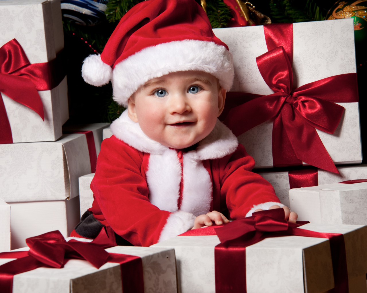 Маленький забавный голубоглазый ребенок в костюме Санты сидит на подарках