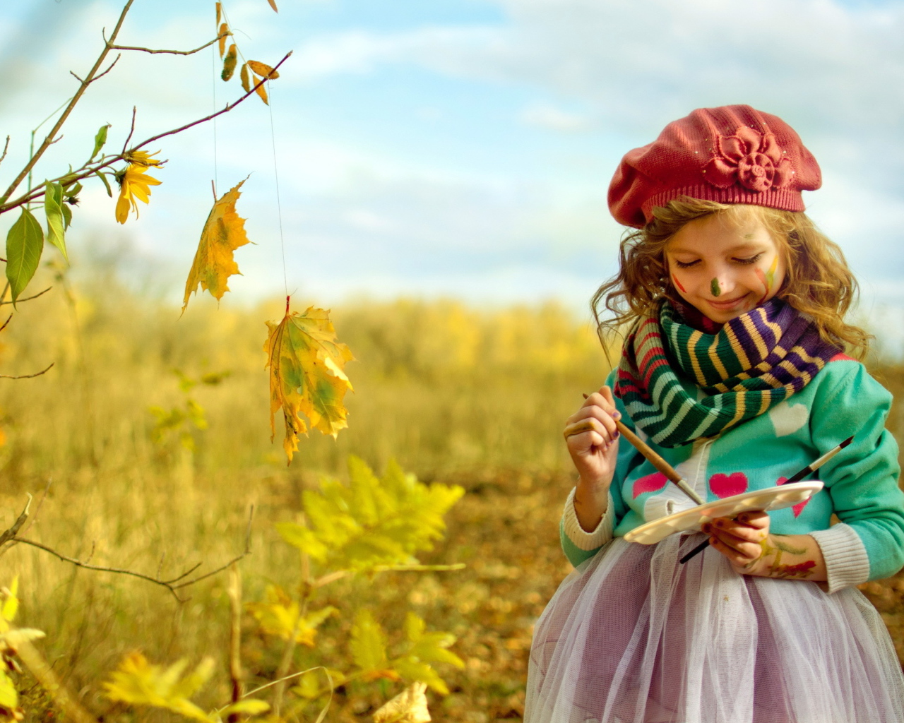 Маленькая девочка рисует красками на листьях осенью 