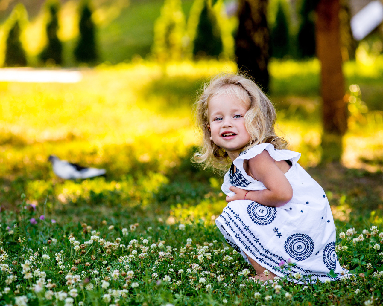 Маленькая девочка в красивом платье сидит на зеленой траве