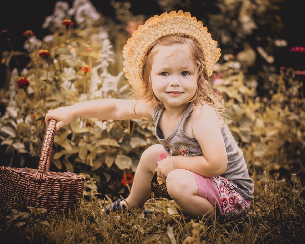 Маленькая девочка в шляпе сидит на траве с корзиной