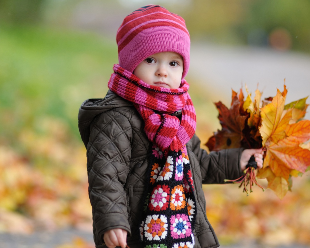 Маленькая девочка в розовой шапке с листьями в руке