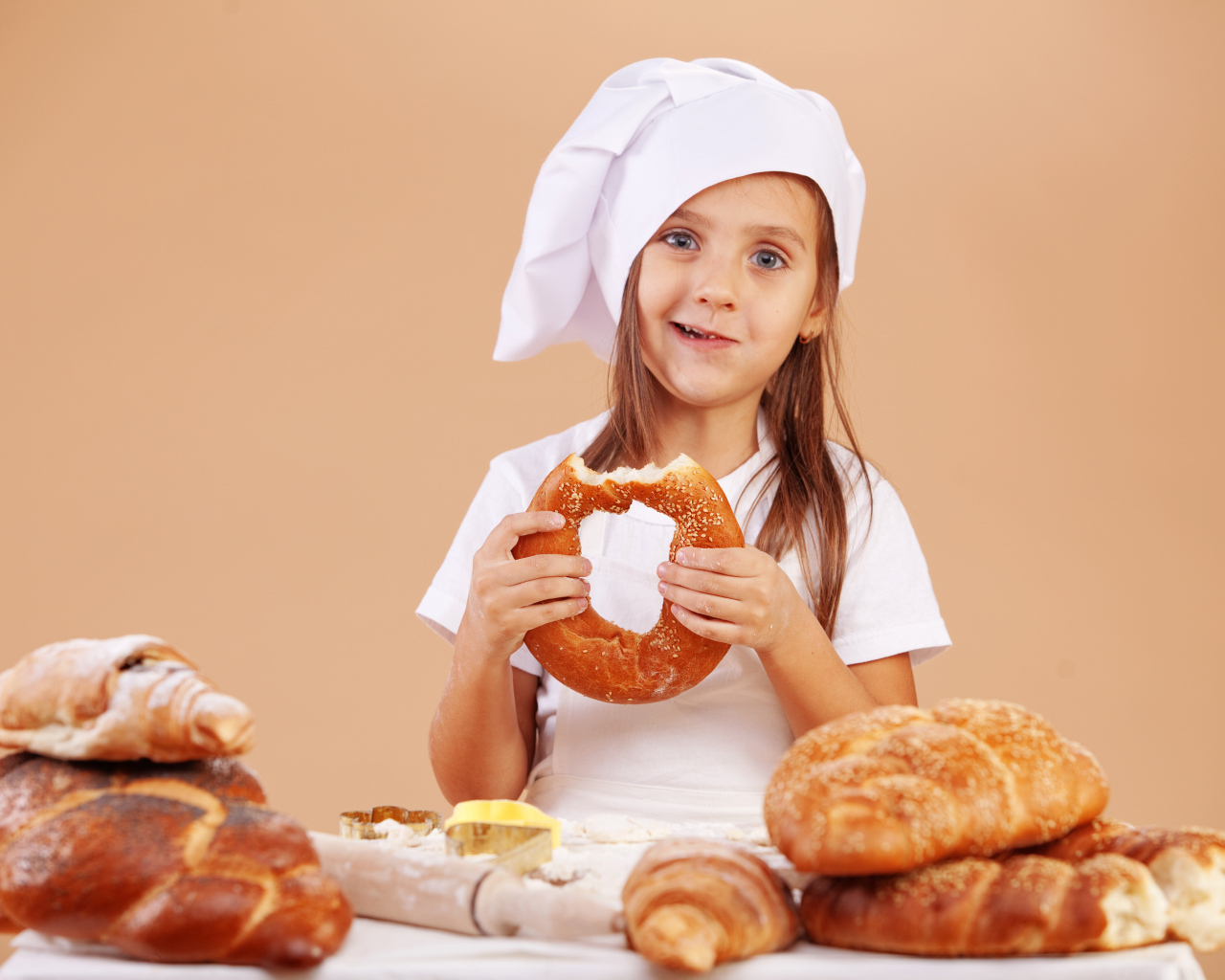 Маленькая девочка в костюме повара и свежей выпечкой