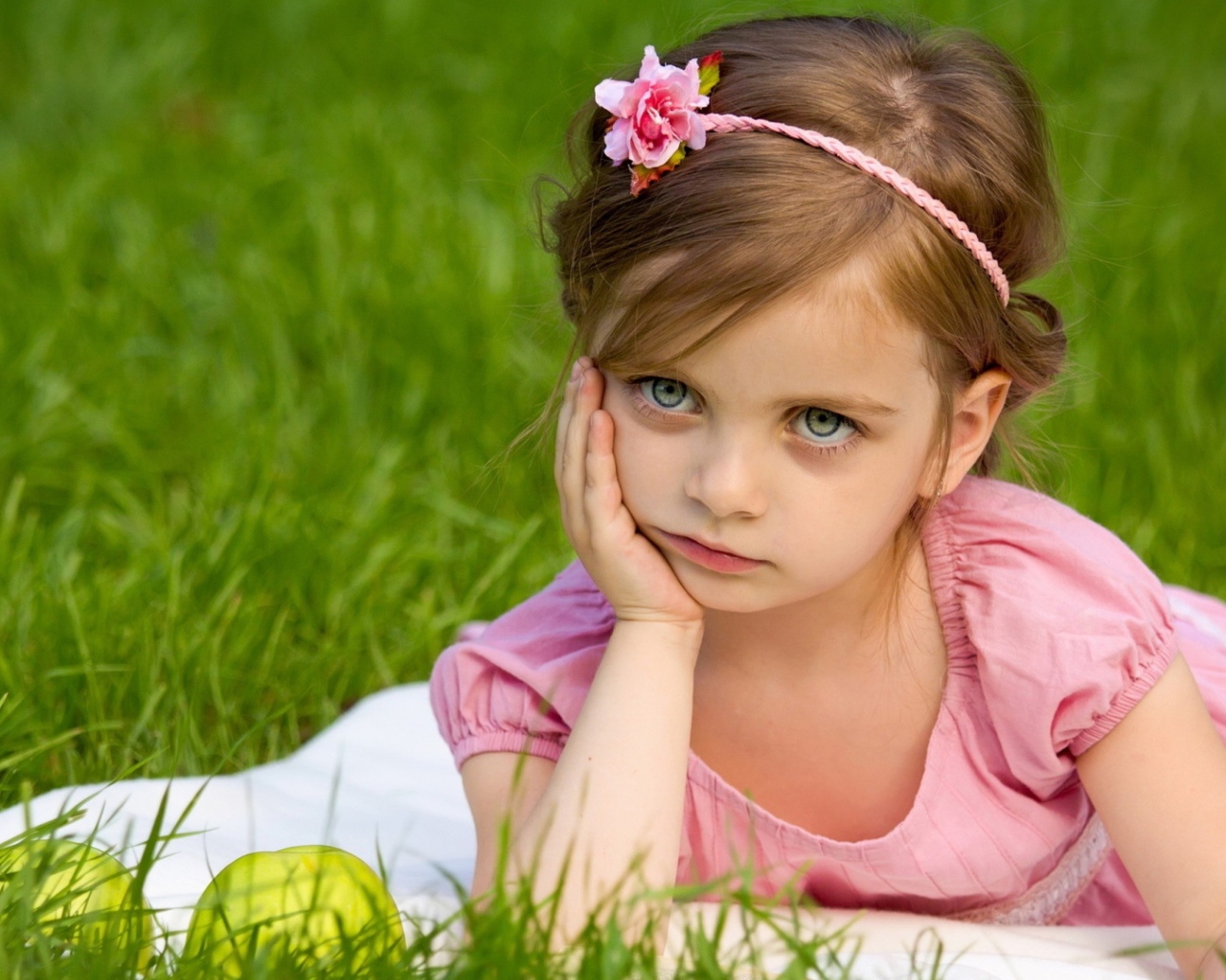 Маленькая девочка в розовом платье лежит на зеленой траве