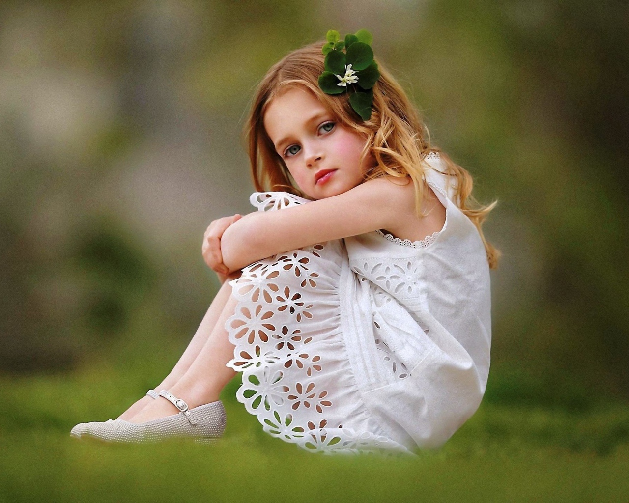 Маленькая девочка в белом платье сидит на зеленой траве