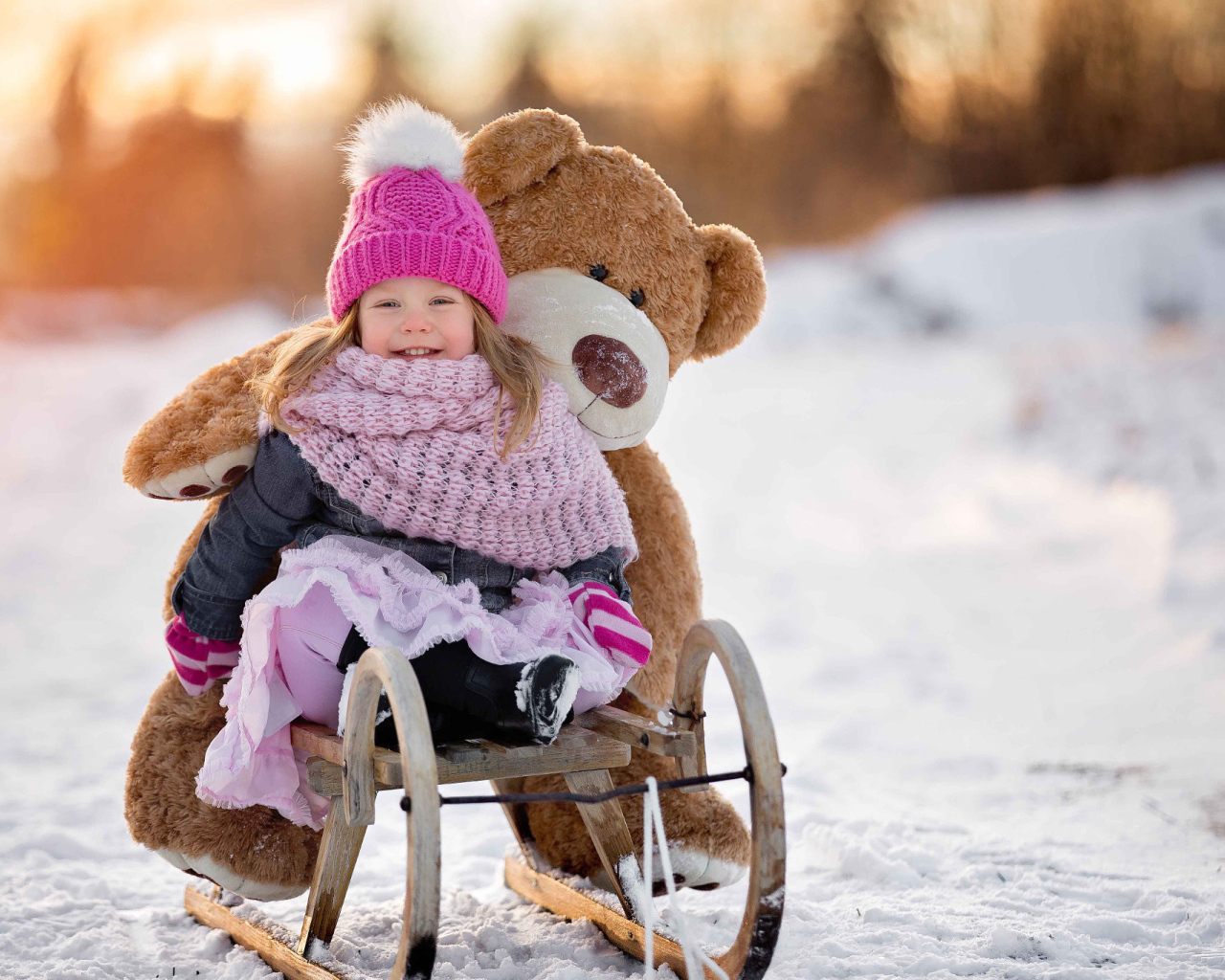 Маленькая девочка на санках с большим медведем зимой 