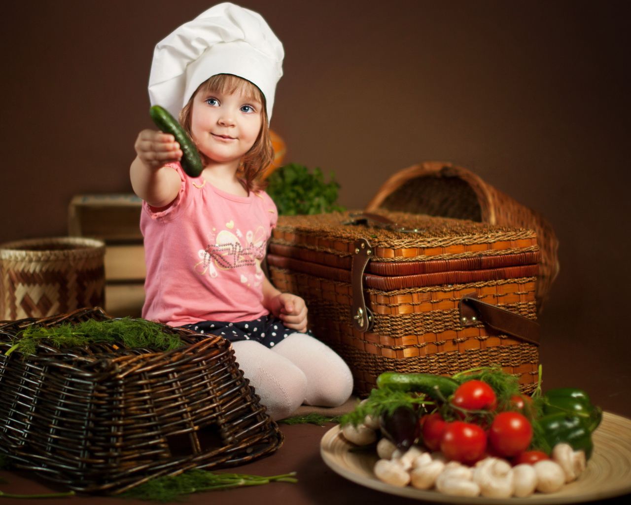 Маленькая девочка сидит на столе с корзинами и овощами