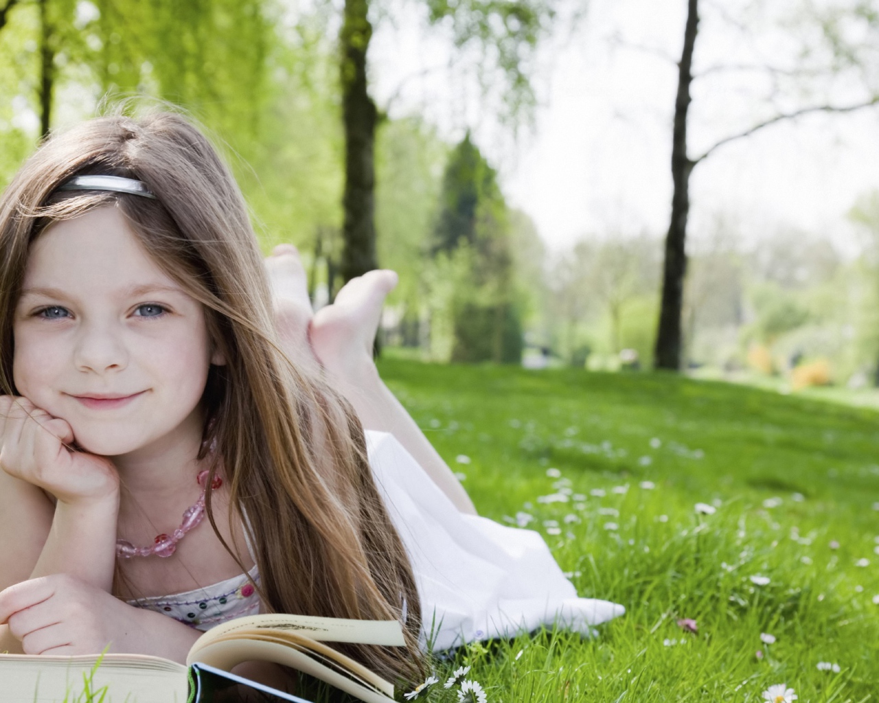 Маленькая девочка с книгой лежит на зеленой траве