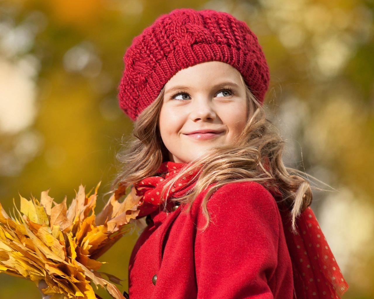 Маленькая девочка с желтыми листьями в руке осенью