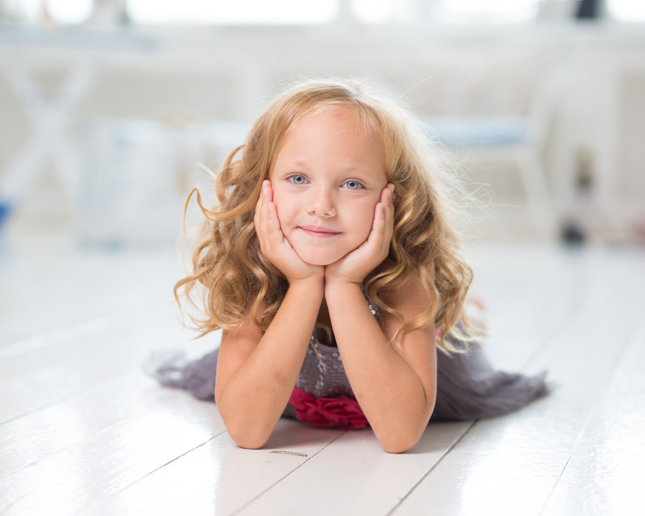 Маленькая длинноволосая голубоглазая девочка лежит на полу