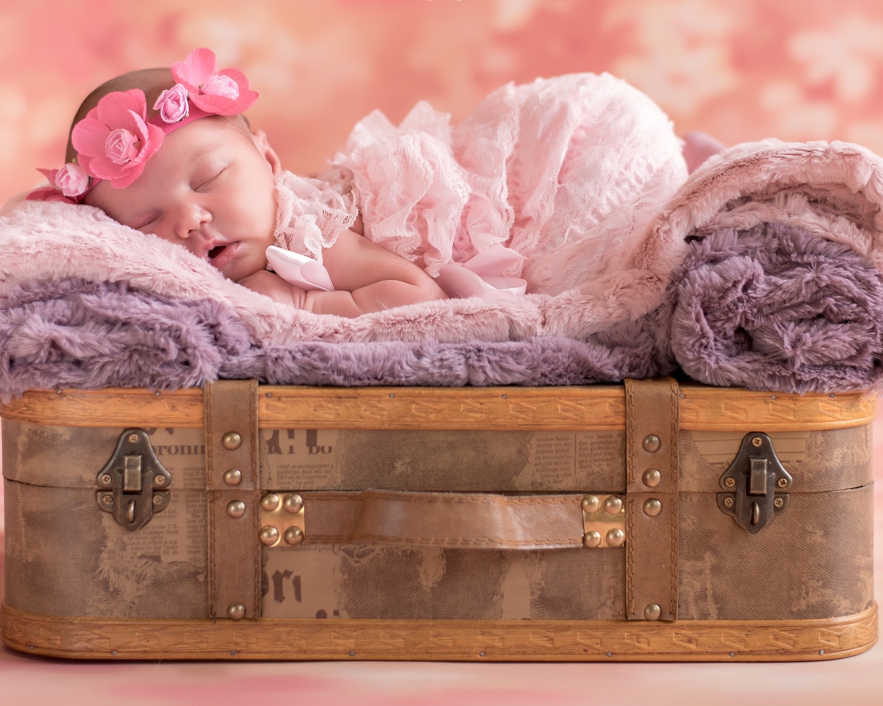 Маленькая новорожденная девочка спит на чемодане
