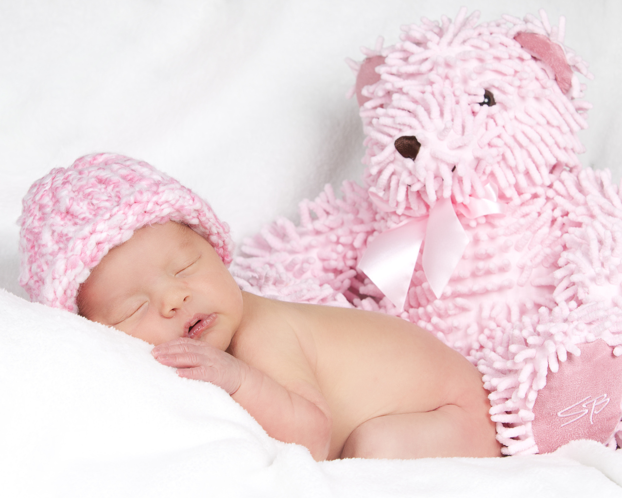 Маленький спящий ребенок в розовой шапке с игрушечным мишкой