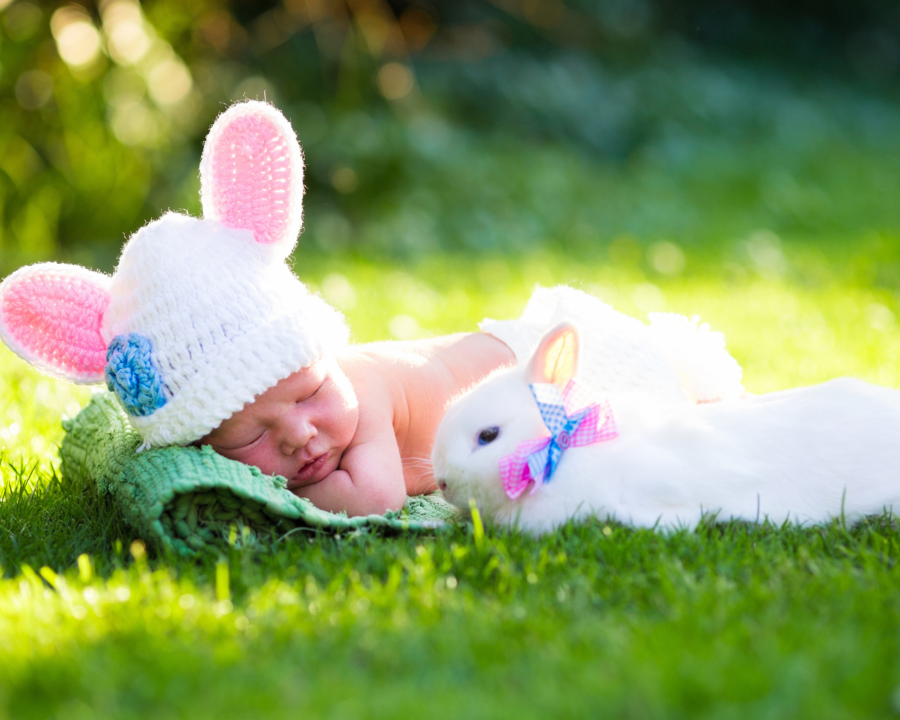 Маленький спящий грудной ребенок на зеленой траве с белым кроликом